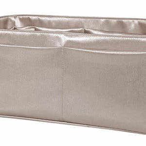 Puede incluir: Organizador de bolso rectangular beige metalizado con dos bolsillos delanteros. El interior y el ribete tienen un acabado satinado. La bolsa est&aacute; dise&ntilde;ada para caber dentro de un bolso tote o un bolso m&aacute;s grande.