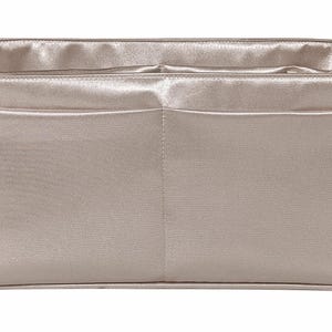 Puede incluir: Organizador de bolso rectangular de color champ&aacute;n claro con dos bolsillos delanteros. El interior es de un tono champ&aacute;n m&aacute;s claro. Fabricado con un material liso similar al sat&eacute;n, dise&ntilde;ado para caber dentro de un bolso m&aacute;s grande.