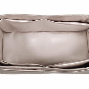 Puede incluir: Un organizador de bolso beige con m&uacute;ltiples compartimentos. El organizador es rectangular con un dise&ntilde;o estructurado, con varios bolsillos interiores para la organizaci&oacute;n. El material parece ser una tela lisa, posiblemente satinada, de color neutro.