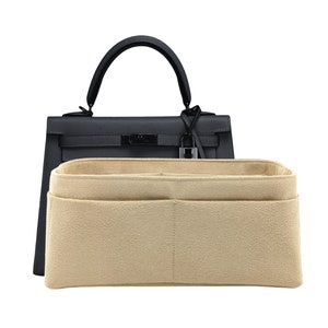 Può includere: Una borsa strutturata grigio scuro con manico superiore e chiusura a lucchetto color argento, posizionata dietro un organizer per borsa in feltro beige dotato di molteplici scomparti interni e tasche aperte per l'organizzazione.