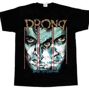 Puede incluir: Camiseta negra con un gráfico de tres caras tras las rejas, la palabra "DRONG" en una fuente goteante encima. El texto "BEG TO DIFFER" está debajo de las caras en azul.