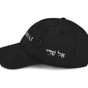 Op de afbeelding: Zwarte distressed baseball cap met witte tekst "UDDAI" op de voorkant en Hebreeuwse tekst aan de zijkant. De cap heeft een gebogen klep en een versleten, vintage uitstraling.