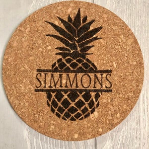 May include: A round cork trivet with a black silhouette of a pineapple and the name "SIMMONS" engraved across the middle.