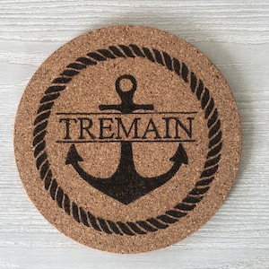 May include: A round cork coaster with a black anchor and rope design. The name "TREMAIN" is written in a banner above the anchor.
