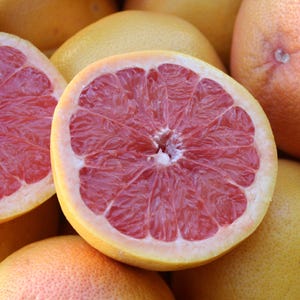 Può includere: Primo piano di diversi pompelmi, alcuni interi e altri tagliati a metà. I pompelmi tagliati rivelano una polpa rosa vibrante, in contrasto con la buccia giallo-arancio. L'immagine mette in risalto la consistenza e il colore del frutto.