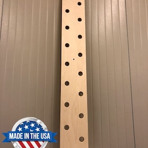 May include: A tall, unfinished wooden board with multiple evenly spaced circular holes. Two wooden dowels rest at the base. The board is made in the USA.