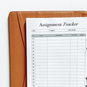 Puede incluir: Un planificador de tareas blanco con una carpeta de cuero marr&oacute;n. El planificador tiene columnas para la clase, la tarea, la fecha de vencimiento y la calificaci&oacute;n. El t&iacute;tulo del planificador es "Assignment Tracker".