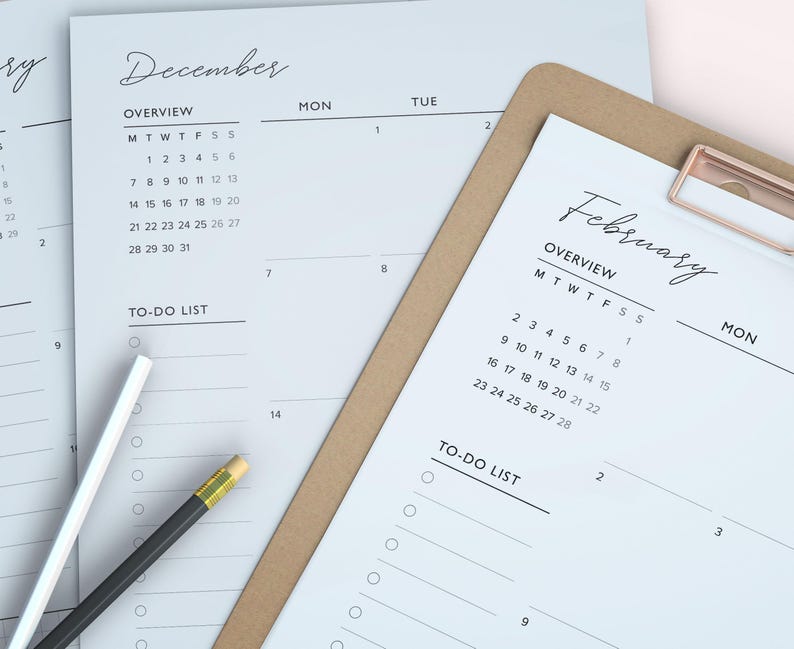 May include: A close-up of a planner with the month of February and December calendars. The planner is on a brown clipboard with a gold clip. A white pencil and a black pencil with a yellow eraser are on the planner.