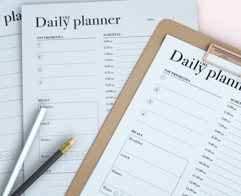 May include: Two white daily planner pages with a brown clipboard on top. The top page has the words "The Daily Planner" and a schedule with times from 6:00 am to 1:00 pm. The bottom page has the words "The Daily Planner" and a schedule with times from 6:00 am to 1:00 pm. Both pages have a section for "Top Priorities" and "Meals".