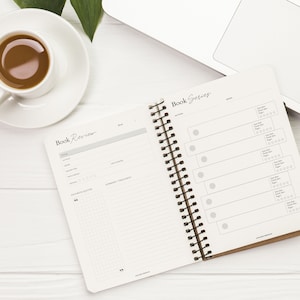 May include: A white notebook with a brown cover and a spiral binding. The notebook is open to two pages, one labeled "Book Review" and the other labeled "Book Series". The pages are filled with blank lines and circles for rating books.
