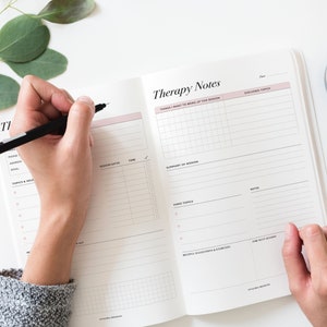 May include: A white and pink therapy notes journal with sections for things to bring up, session dates, time, summary of session, hard topics, notes, helpful suggestions and exercises, and for next session. The journal is open and a person is writing in it with a black pen.