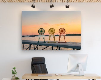 May include: A modern office space with a desk, chair, and a large canvas print of three colorful chairs on a dock overlooking a lake at sunset.