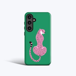 May include: A green phone case featuring a pink cheetah design with black spots. The cheetah is in a seated position with its tail curled. The phone case has a camera and flash module on the upper left side.