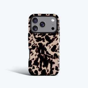 May include: A smartphone case featuring a tan background with an irregular black cow-print pattern. The case has a rectangular cutout at the top for a triple-lens camera system and a flash, with a black border surrounding the camera module area.