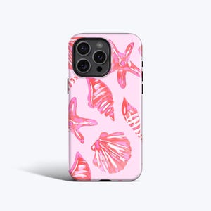 Puede incluir: Funda de teléfono rosa con un diseño de acuarela de conchas marinas y estrellas de mar en tonos rosas y rojos. La funda tiene un acabado brillante y un módulo de cámara negro.