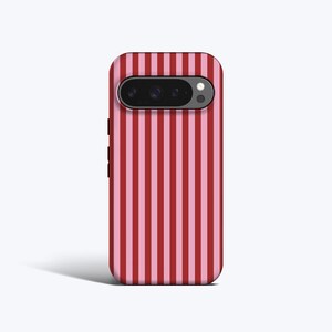 Könnte beinhalten: Eine Smartphone-Hülle mit vertikalem Streifenmuster in abwechselnden Rot- und Rosatönen. Die Hülle hat einen Kamera- und Blitz-Ausschnitt oben und eine schwarze Ein-/Aus-Taste an der Seite.