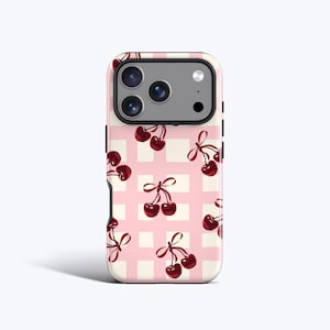 Op de afbeelding: Een telefoonhoesje met een roze en wit geblokt patroon, versierd met illustraties van kersen. De kersen zijn dieprood met groene steeltjes en rode strikken. De hoes heeft een camera-uitsparing en een witte rand.