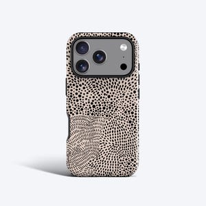 Könnte beinhalten: Eine Smartphone-Hülle mit beigem Hintergrund und einem dichten, sich wiederholenden Muster aus kleinen schwarzen Punkten und kurzen, geschwungenen schwarzen Linien. Die Hülle hat eine rechteckige Aussparung für eine Dreifachkamera und Blitz.