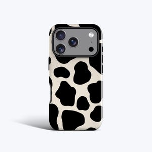 May include: A smartphone case featuring a black and white cow print design. The case has a black border and a camera cutout. The pattern consists of irregular black spots on a cream background, offering a fun aesthetic.