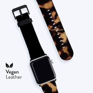 Könnte beinhalten: Ein schwarzes und braunes gemustertes veganes Lederarmband mit einem silbernen Zifferblatt. Das Armband ist an einem schwarzen Lederarmband mit einer Schnalle befestigt. Der Text "Vegan Leather" ist unter einem Blattsymbol gedruckt.