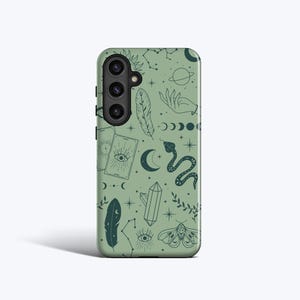 Op de afbeelding: Saliegroene telefoonhoes met een herhalend patroon van hemelse en mystieke elementen. Het ontwerp bevat een zon, sterrenbeelden, een hand, veren, tarotkaarten, een slang, een kristal, een mot en halve manen.