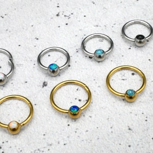 Peut inclure: Assortiment de boucles d'oreilles créoles en or et en argent avec des pierres opalescentes colorées. Les créoles sont de tailles différentes et ont une fermeture à boule.