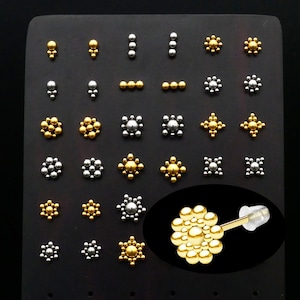 May include: A display of gold and silver stud earrings with various designs, including circles, squares, and stars. The earrings are arranged on a black background.