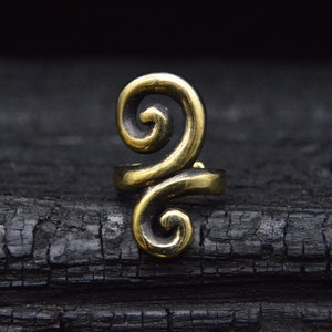 May include: A gold-colored metal ring with a swirling design. The ring is on a black background.