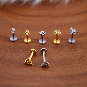 Può includere: Un set di sette gioielli per il corpo in oro e argento. I gioielli sono a forma di stella, cerchio e fiore. I gioielli sono su una superficie di legno.