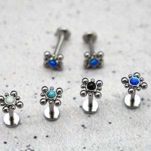 May include: Six different styles of surgical steel body jewelry with various colored gemstones. The jewelry is in the shape of a small square with a round gemstone in the center.
