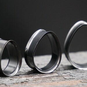 May include: Three black and silver ear gauges of different sizes. The gauges are shaped like ovals with a slightly pointed top and bottom.