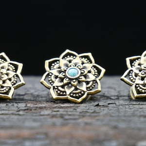Könnte beinhalten: Drei goldfarbene Ohrstecker aus Metall mit einem türkisfarbenen Stein in der Mitte jedes Steckers. Die Stecker sind blumenförmig mit filigranen Details.