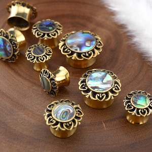 Może przedstawiać: Zestaw rozpychaczy do uszu z mosiądzu z wkładkami z muszli abalone. Rozpychacze mają ozdobny, falisty brzeg.