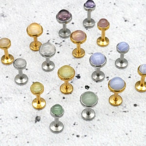 Op de afbeelding: Assortiment van 16 lichaamssieraden met edelstenen. De sieraden zijn gemaakt van roestvrij staal en goud. De edelstenen zijn in verschillende kleuren, waaronder blauw, groen, roze, paars en wit.