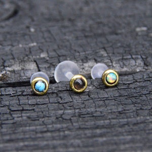 Op de afbeelding: Drie gouden lichaamsieraden met verschillende gekleurde edelstenen. De edelstenen zijn turquoise, zwart en regenboogkleurig.