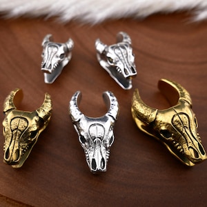 Puede incluir: Cuatro abalorios de cráneo de toro en plata y oro con detalles intrincados. Los abalorios tienen forma de cabeza de toro con cuernos y un diseño de cráneo detallado. Los abalorios son perfectos para añadir un toque de estilo rústico a las joyas u otras manualidades.