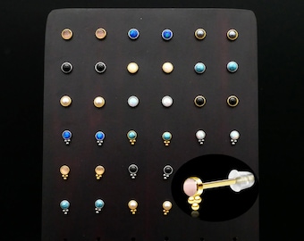 May include: A display of various colored and textured round studs for jewelry making. The studs are arranged in rows on a black background. The studs are made of different materials, including metal, glass, and plastic. The studs are available in a variety of colors, including black, white, gold, blue, and turquoise.