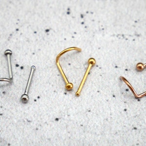 May include: Three nose rings with ball ends. One is gold, one is silver, and one is rose gold.