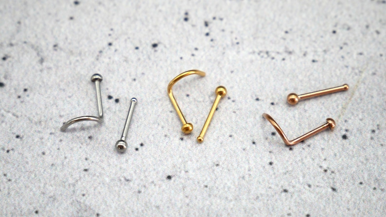 May include: Three nose rings with ball ends. One is gold, one is silver, and one is rose gold.