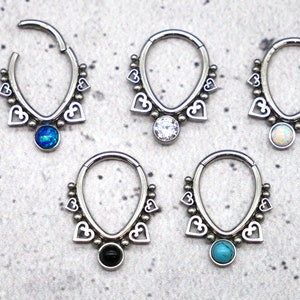 Puede incluir: Cinco pendientes de aro de plata con un dise&ntilde;o de coraz&oacute;n y una piedra preciosa colgante. Las piedras preciosas son azul, blanco, &oacute;palo, negro y turquesa.