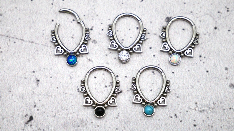 Puede incluir: Cinco pendientes de aro de plata con un dise&ntilde;o de coraz&oacute;n y una piedra preciosa colgante. Las piedras preciosas son azul, blanco, &oacute;palo, negro y turquesa.