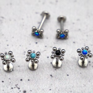 May include: Six silver body jewelry pieces with a small round gem in the center of a flower-shaped design. The gems are turquoise, black, white, and blue.
