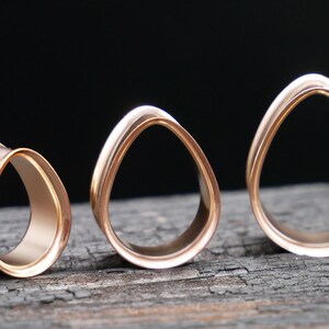 May include: Three rose gold ear gauges in different sizes. The gauges are shaped like an oval with a smooth, polished finish.