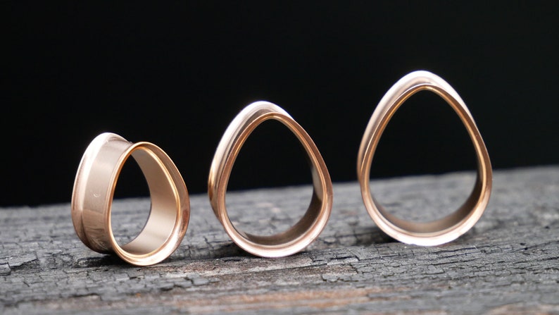 May include: Three rose gold ear gauges in different sizes. The gauges are shaped like an oval with a smooth, polished finish.