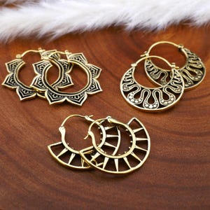 May include: Set of four gold-toned hoop earrings with intricate geometric designs. The earrings feature a variety of patterns, including floral, wave-like, and sunburst motifs.