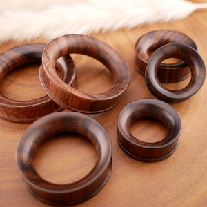 May include: A collection of five circular ear gauges crafted from dark brown wood with visible grain patterns. The gauges feature a smooth, polished finish and a hollow center, varying in size from smaller to larger diameters for ear stretching.