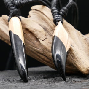 Könnte beinhalten: Zwei schwarze und naturfarbene Holzanhänger mit einem schwarzen Band. Die Anhänger sind in Form einer langen, dünnen Träne geformt.