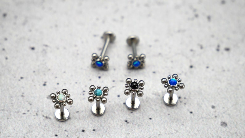 May include: Six different styles of surgical steel body jewelry with a variety of colored gemstones. The jewelry is in the shape of a small flower with a single gemstone in the center.
