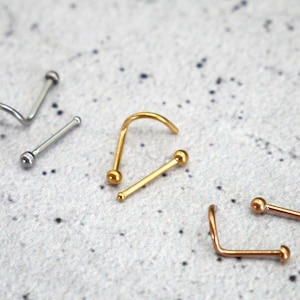May include: Four nose rings with ball ends. Two are silver, one is gold, and one is rose gold.