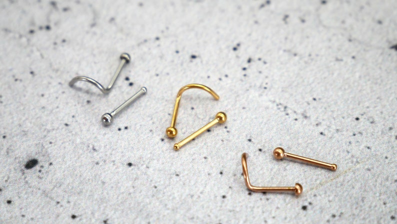May include: Four nose rings with ball ends. Two are silver, one is gold, and one is rose gold.